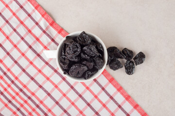 Dry black plums in a ceramic cup on concrete background