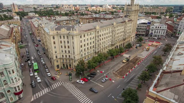 Constitution Square with historical buildings aerial timelapse in Kharkiv, Ukraine. Traffic on road intersection and excavator on a road construction site near house with a spire. View from rooftop