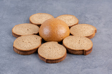 Circle of brown bread slices around a single bun on marble background