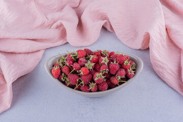 Pink tablecloth behind a small bowl of raspberries on marble background