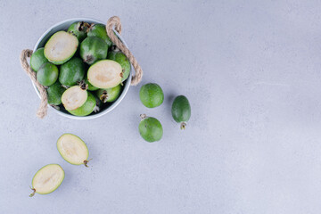 White bucket filled with fresh feijoas on marble background