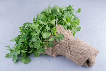 Fresh bundle of parsley wrapped in a piece of cloth on marble background