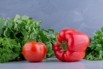 Bell pepper and tomato in front of piles of mint, parsley, coriander and dill on marble background