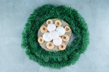 Garland wrapped around a board with cookies and dry apple slices on marble background