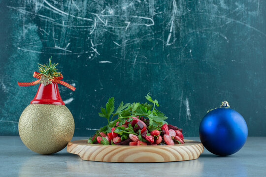 Festive baubles next to a platter of parsley topped vinegret salad on marble background
