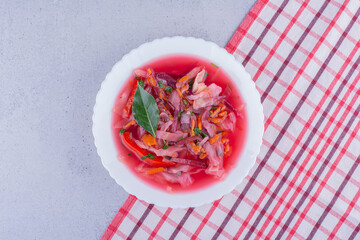 Bowl of borsch soup with a bay leaf topping on a tablecloth on marble background