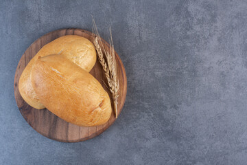 Two buns and a single wheat stalk on a wooden board on marble background