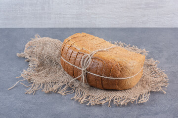 Tied-up block of sliced bread on a piece of cloth on marble background - obrazy, fototapety, plakaty