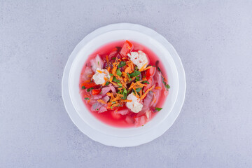 Serving of borsch soup with carrot and cauliflower topping on marble background