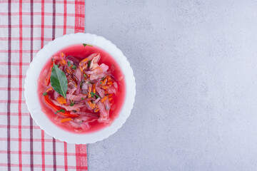 Piping hot bowl of borsch soup with a bay leaf topping on a tablecloth on marble background