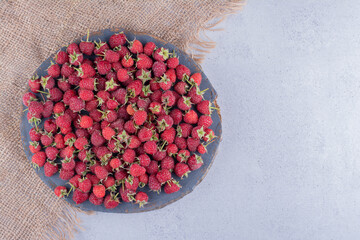 Piece of cloth under a pile of raspberries on a wooden board on marble background