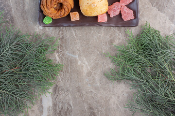 Marmelades, almond wrap and a cookie on a platter next to pine branches on marble background