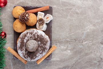 Chocolate powder coated donut, cinnamon sticks, cookies, lokums and pine cones on marble background