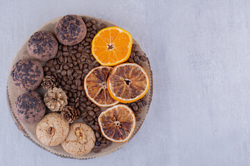 Assortment of dry and juicy orange slices, coffee beans, pine cones and cookies on a board on white background