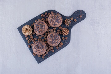 Black board with coffee beans, cookies, and pine cones on white background