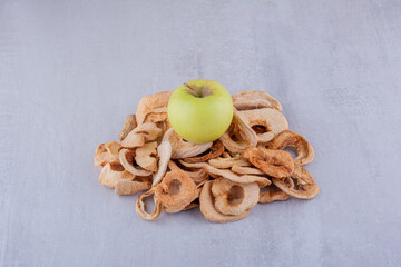 Small heap of dried apple slices with a whole apple sitting on top on white background