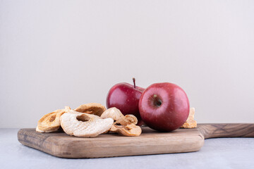Apples and dried apple slices on a board on white background