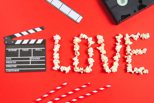 Movie clapperboard, film strip, videotapes, straws and the word love from popcorn lie on a red