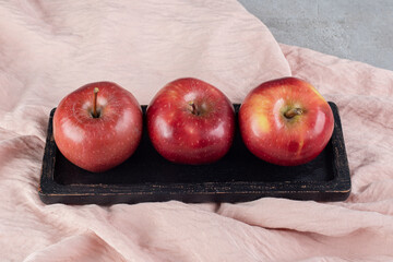 Wooden platter of three apples on textile background