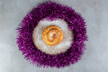 Coconut powder covered trivet with a bun in a garland circle on marble background
