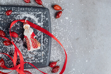 Wooden tray. hips, red ribbons, scissors, coconut powder and santa figurine on marble background