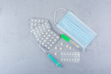 Thermometer, mask, syringe and medical pills on marble background