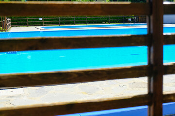 Selective focus. swimming pool water on a sunny day across a wooden fence. Water surface. Hotel resort. Summertime activities