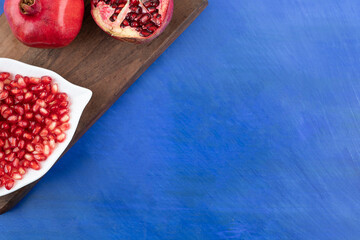 A wooden cutting board full of pomegranate on blue background