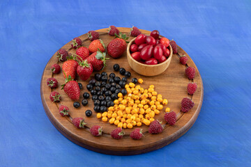 A wooden board full of berries on blue background