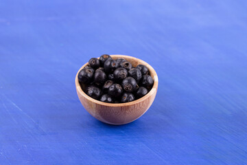 Fototapeta na wymiar A small wooden bowl full of blackcurrant on blue background