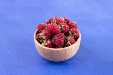 A wooden bowl full of raspberries on blue background