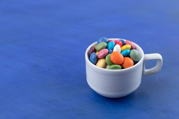 A white cup full of candies on blue background