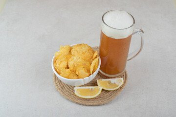 Glass of beer with lemon slices and bowl of chips on stone table