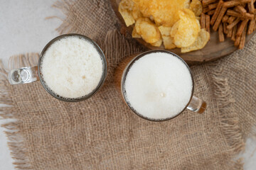 Two foamy beers and snack plate on burlap