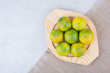 Full wooden plate of sour tangerines on white background