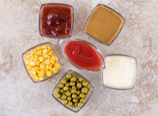 Arrangement of green peas, corn kernels, ketchup, mayonaisse, mustard and red sauce on marble background
