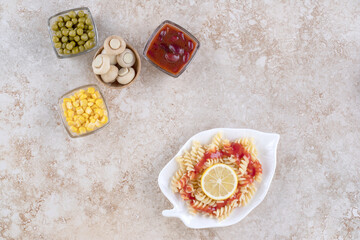 Salad ingredients displayed next to a plate of macaroni on marble background