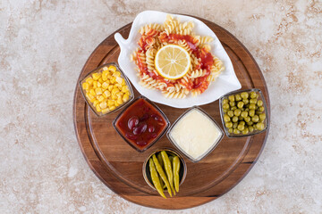 Tray with pasta serving and bowls of toppings and dressings on marble background