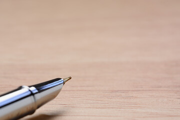 Silver fountain pen on light brown wooden table background.