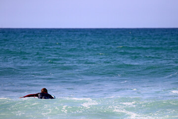 A surfer in the sea near the coast, lying on the surfboard