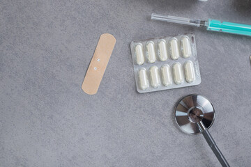 Blister with white pills and empty syringe on gray background