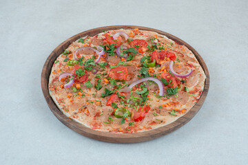 A wooden plate of pita bread with sliced tomato and onion