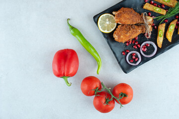 A black plate full of fried chicken with tomatoes and pepper