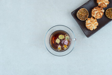 A cup of herbal tea with cookies and dried oranges on black plate