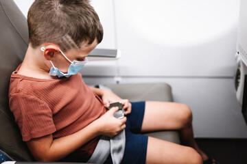 Boy in face mask fastening safety belt inside plane