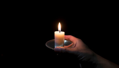 A hand of a man holding a lit candle in the dark.