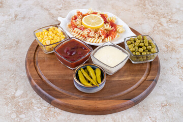 Wooden tray with pasta serving and bowls of toppings and dressings on marble background
