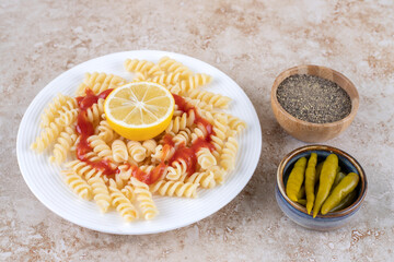 Platter of macaroni with small bowls of black pepper and pickled peppers on marble background