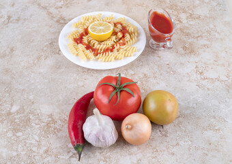 Macaroni portion and a sauce glass of ketchup with assorted vegetables on marble background