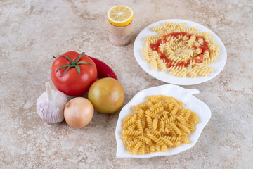 Various vegetables next to macaroni platters on marble background